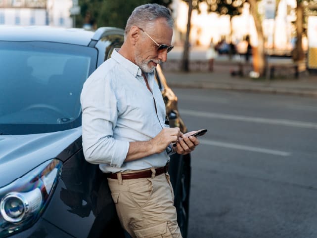 Usuario apoyado en un coche, consultando el móvil