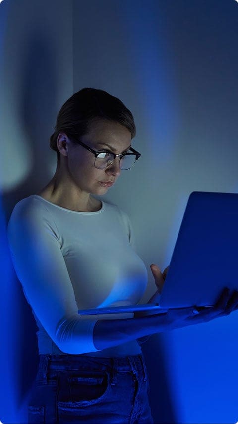 Woman leaning against a wall holding a laptop